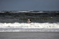Ein Mann mit Hut und einem Kind auf dem Arm geht den Wellen der Nordsee entgegen (A man with a hat and a child in his arms is walking towards the waves of the North Sea)